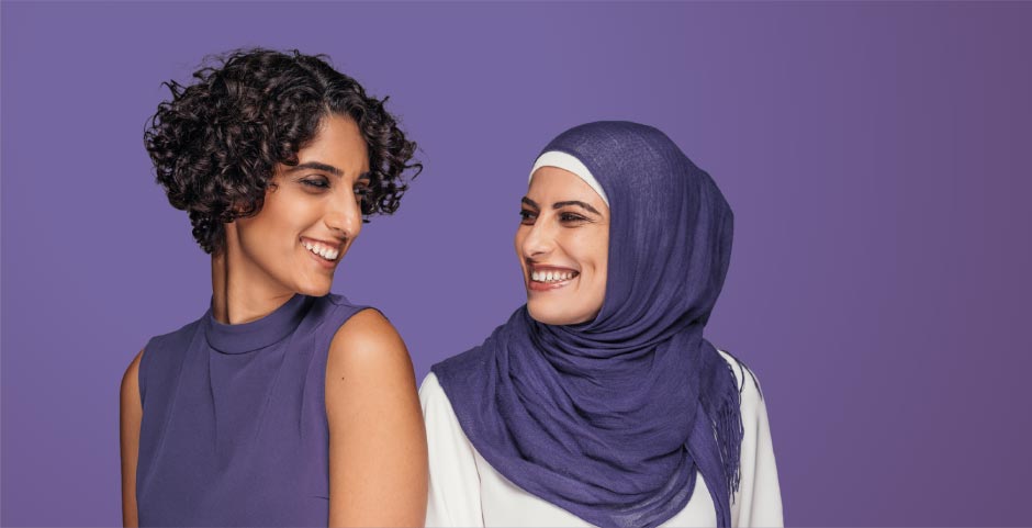 Picture of two women smiling at each other against a purple background.